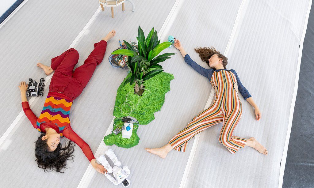 Zwei Tänzerinnen des Studio Sucrow liegen auf einer Bühne mit einer Pflanze in der Mitte