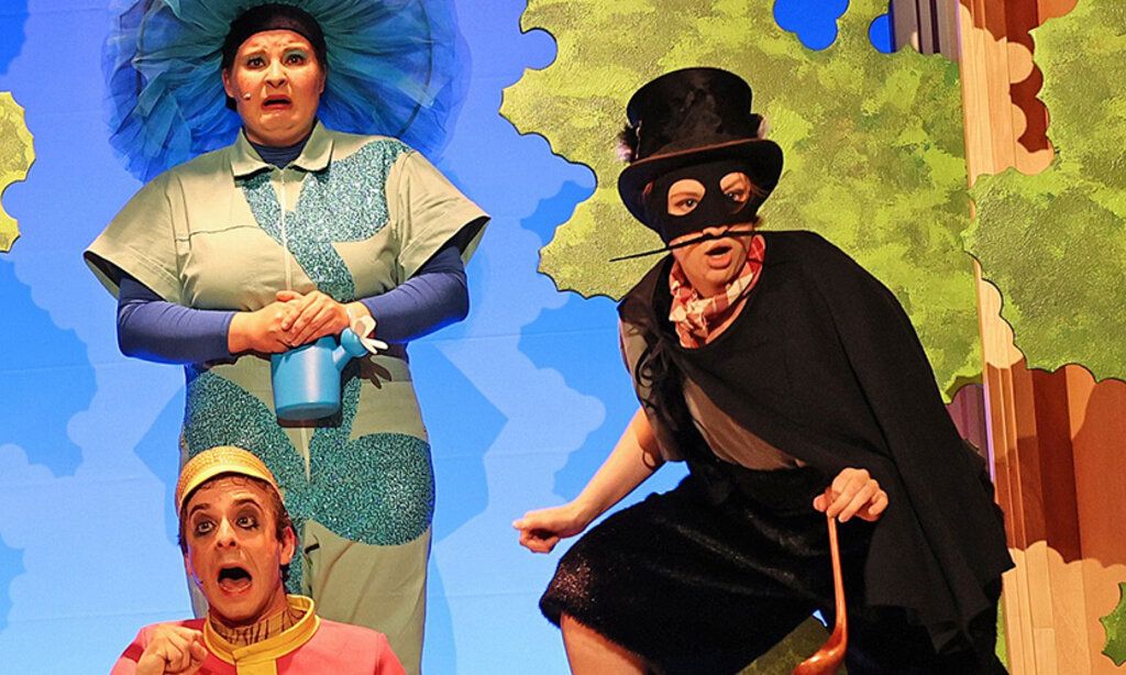 Schauspieler der Burghofbühne Dinslaken spielen vor einer Kulisse von Bäumen und blauem Himmel.