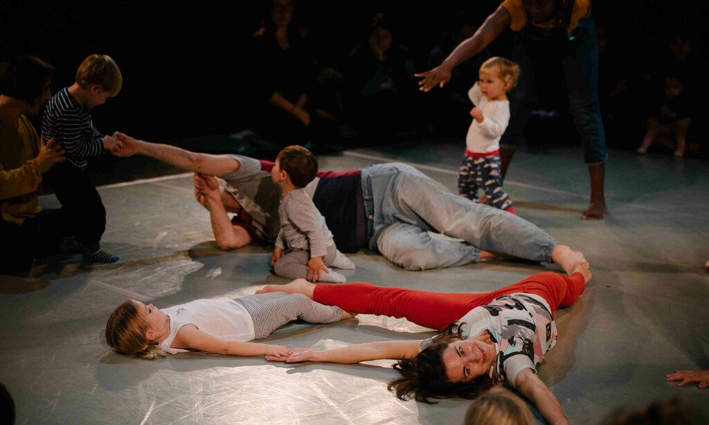 Drei Tänzer:innen tanzen mit kleinen Kindern auf dem Bühnenboden.