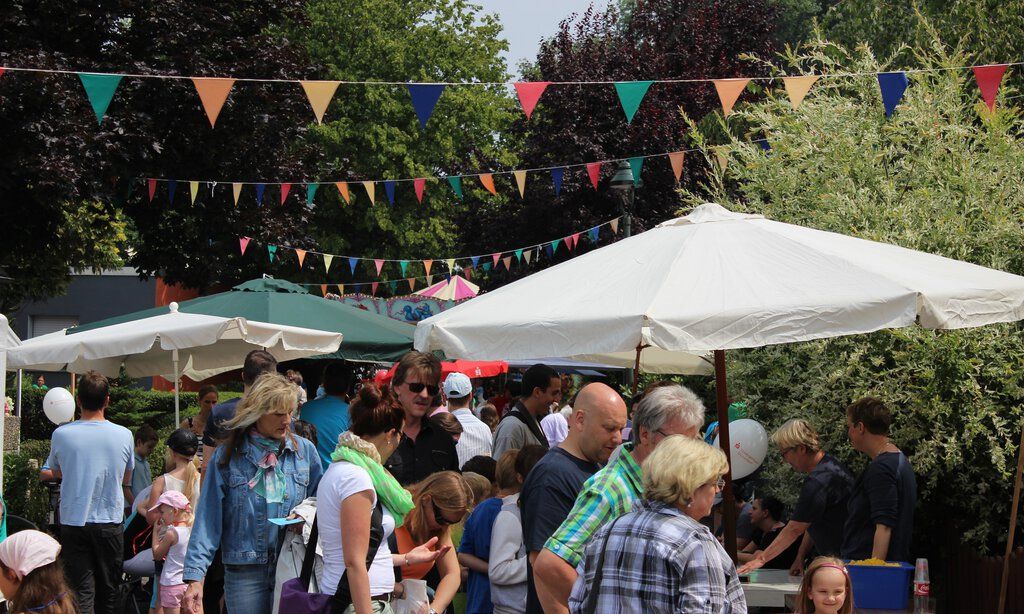 Besucher des Straßenfests in der Tannenhofsiedlung Vennhausen spazieren an bunt geschmückten Ständen vorbei.
