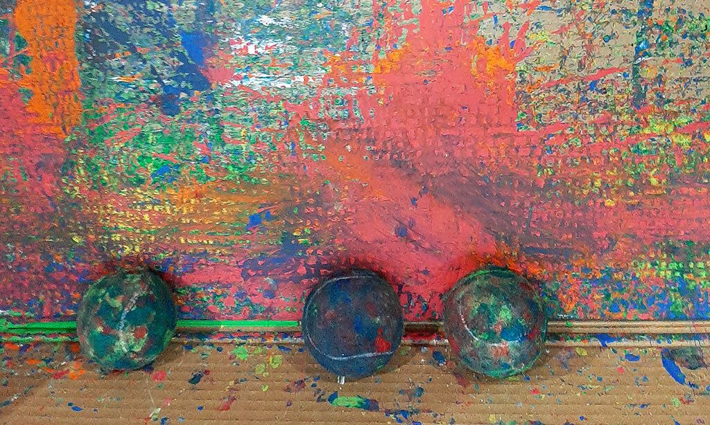 Drei in Farbe getränkte Tennisbälle liegen vor einer bun bemalten Wand.