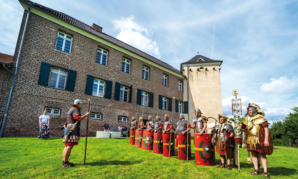 Männer in römischen Rüstungen stehen auf einer Wiese vor haus Bürgel