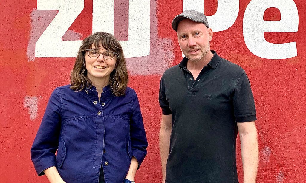 Porträt von Alexandra Wehrmann Sven Andre Dreyer vor einer roten Wand mit weißen Buchstaben