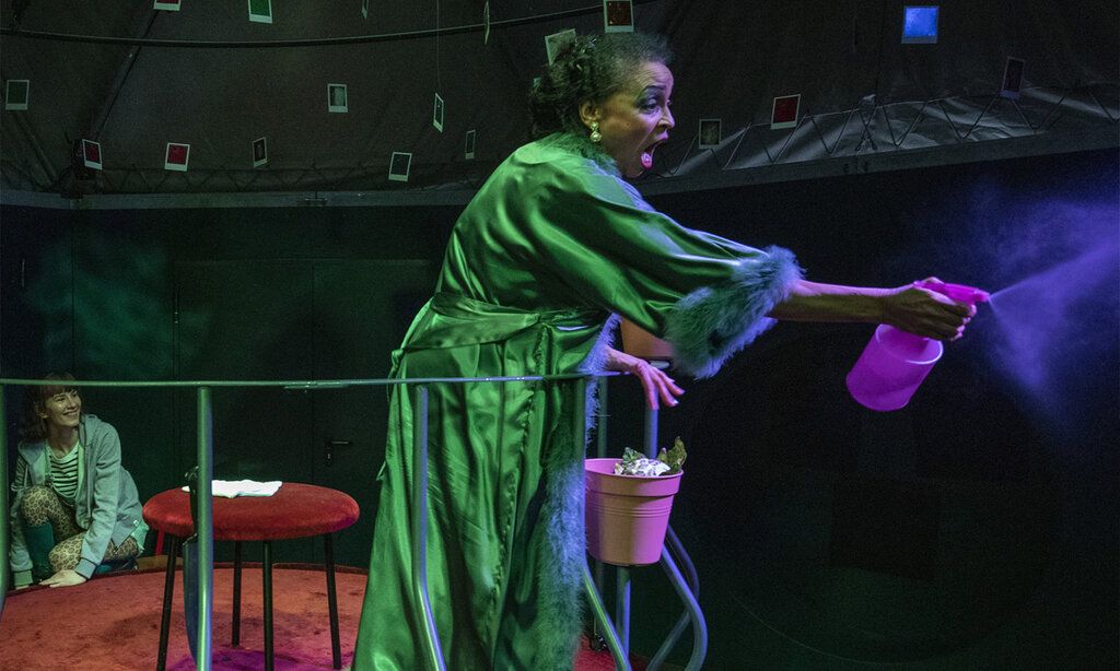 Eine Schauspielerin sprüht mit einer Sprühflasche herum, dunkle Stimmung