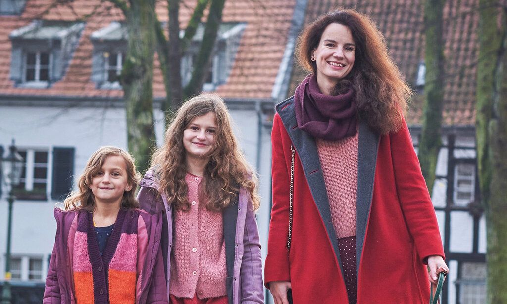 Anna Vogel mit ihren beiden Töchtern in Gerresheim, im Hintergrund ein Haus und ein Fachwerkhaus und kahle Bäume