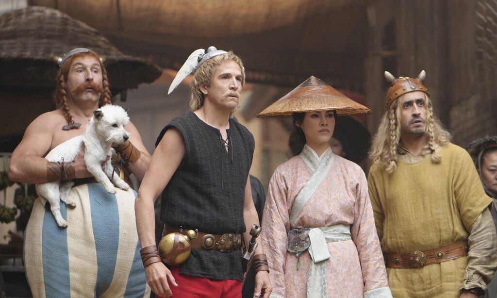 Asterix und Oberlix stehen zusammen mit einer Chinesin und einem Wikinger, Obelix trägt Hund Idefix auf dem Arm, alle gucken überrascht
