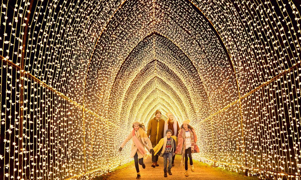 Eine Familie mit drei Kindern in Winterkleidung läuft gemeinsam durch einen mit Licherketten illuminierten Tunnel.