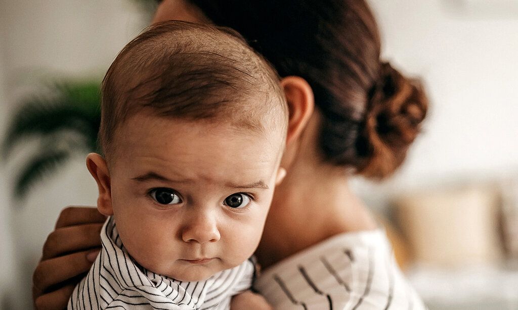 Baby ist bei der Mutter auf dem Arm und guckt kritisch in die Kamera