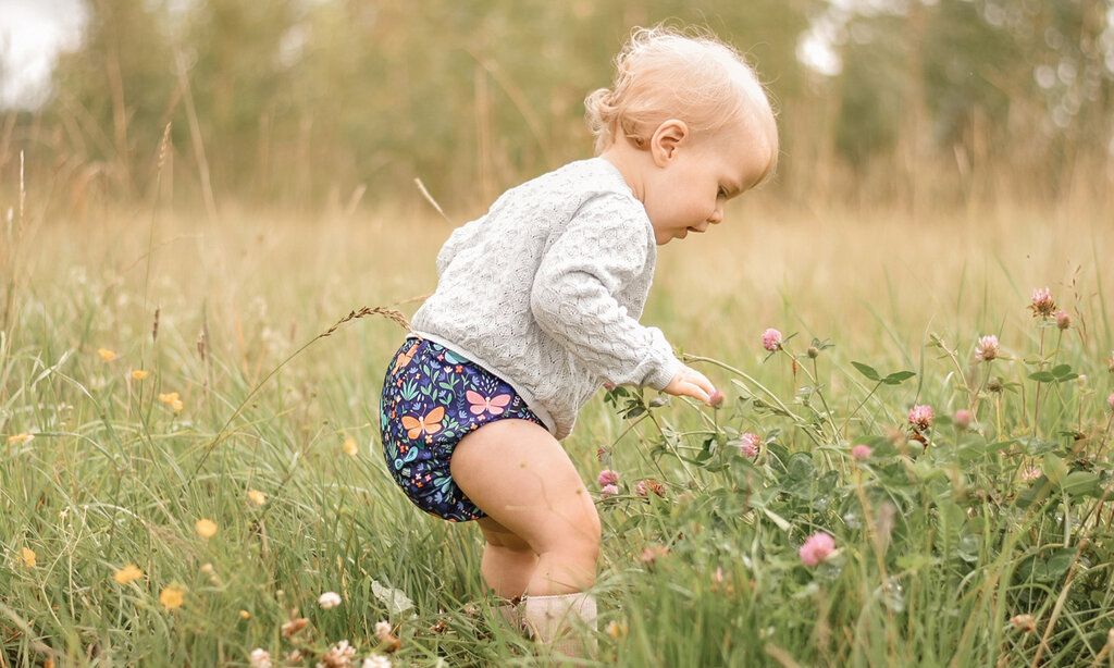 Baby mit Stoffwindel steht auf Blumenwiese
