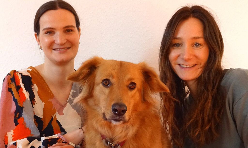 Porträt von zwei Frauen und einem Hund, im Hintergrund Raufasertapete