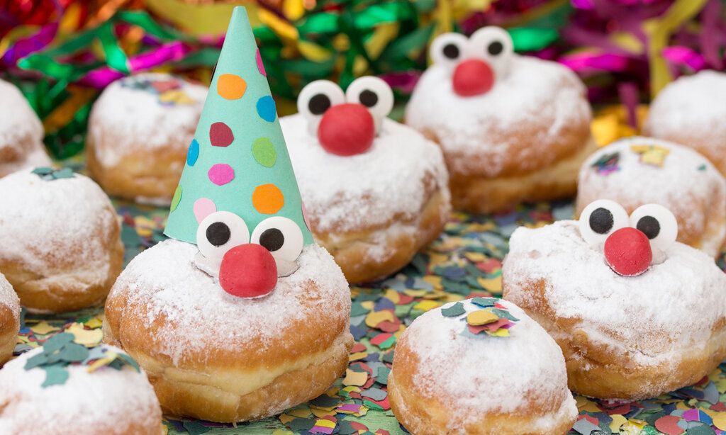 Karnevalsgebäck Berliner mit Augen und Nasen und Hütchen, auf Tisch mit Konfetti und Luftschlangen