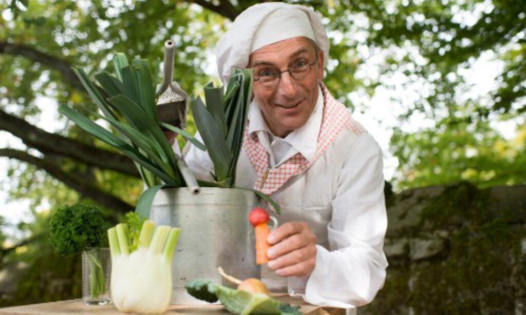 Der Märchenkoch in Kochuniform mit einem Kochtopf und Gemüse.