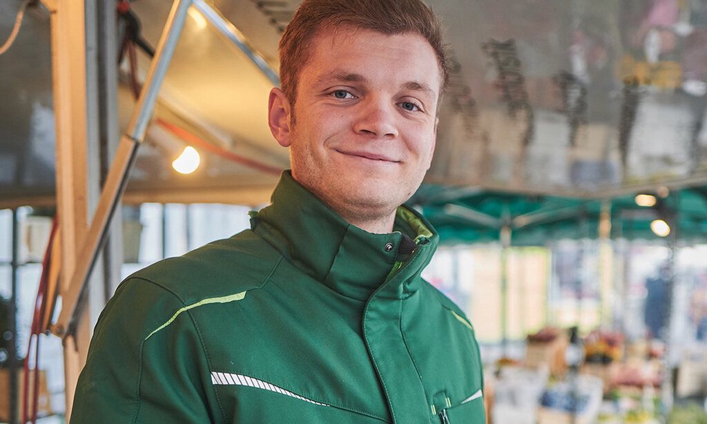 Junger Händler steht auf dem Markt lächelt in die Kamera
