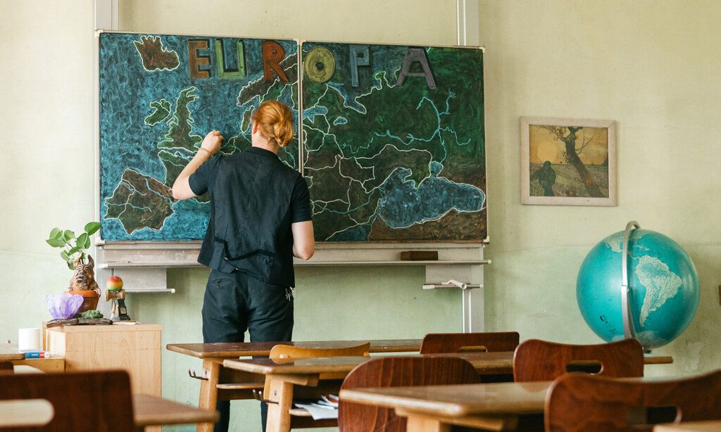 Ein Lehrer steht in einem Klassenzimmer und zeichnet eine Europa-Karte an die Tafel