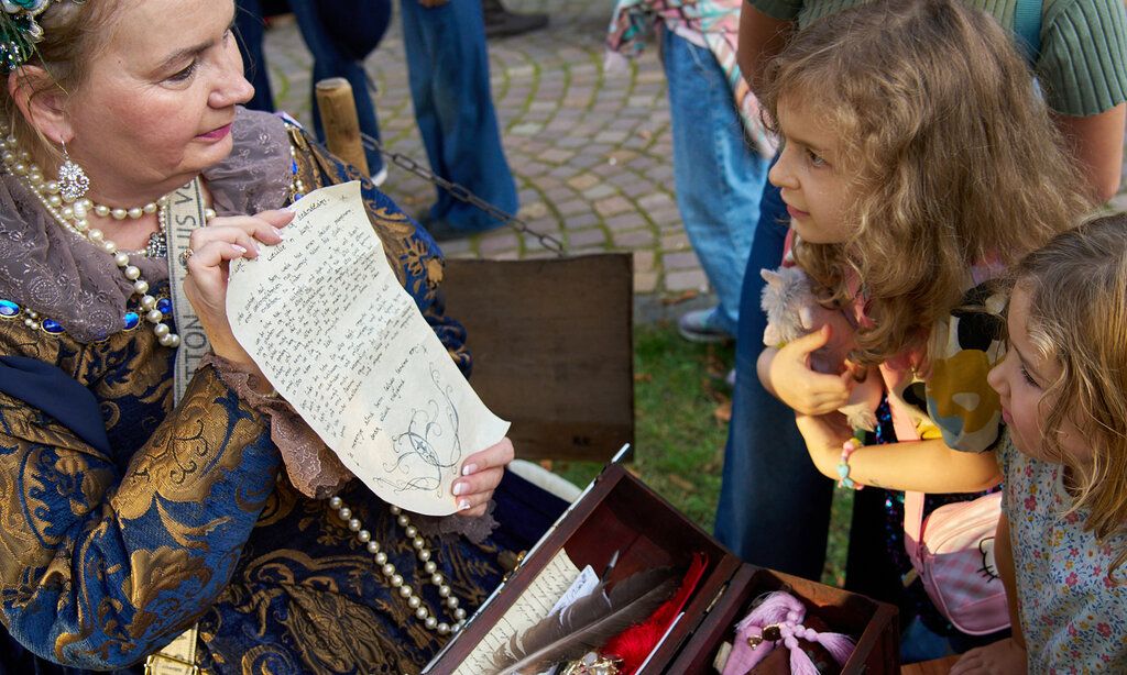 Eine Frau ist als Charlotte von Aschenberg verkleidet und zeigt zwei Mädchen ein Schriftstück im Kindermuseum Adlerturm