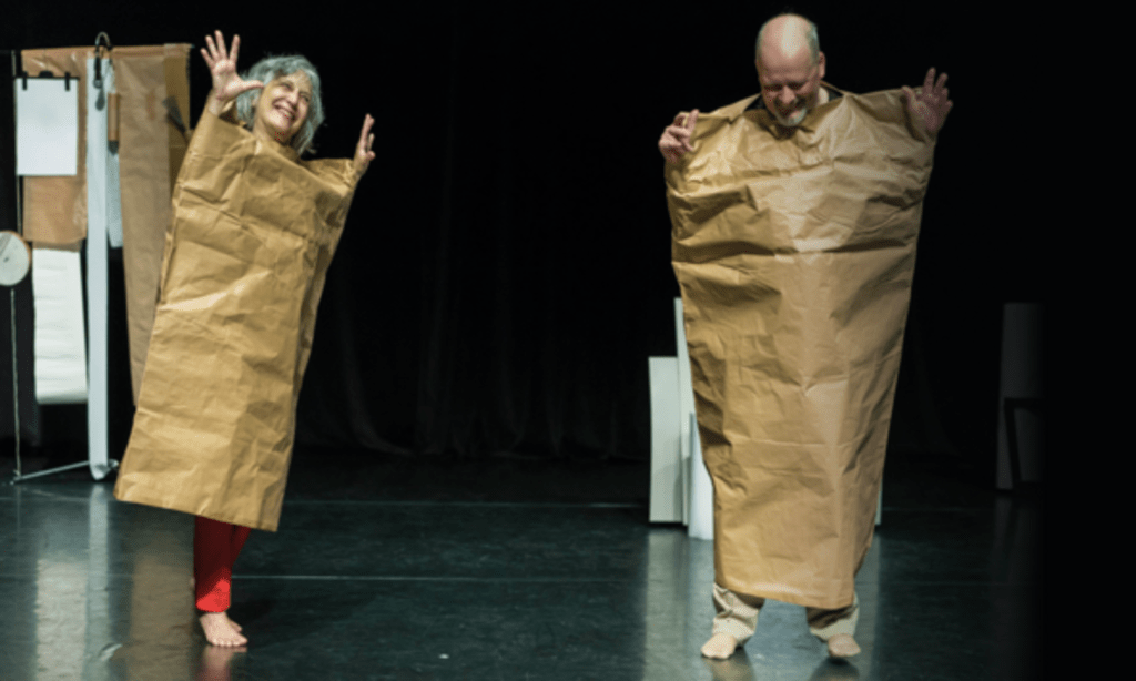 Zwei Schauspieler auf einer Bühne sind in große Papiertüten eingewickelt.