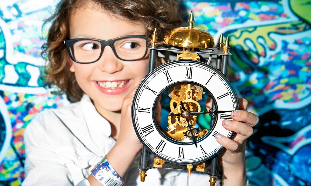 Mädchen mit großem Wecker vor einer bunten Wand