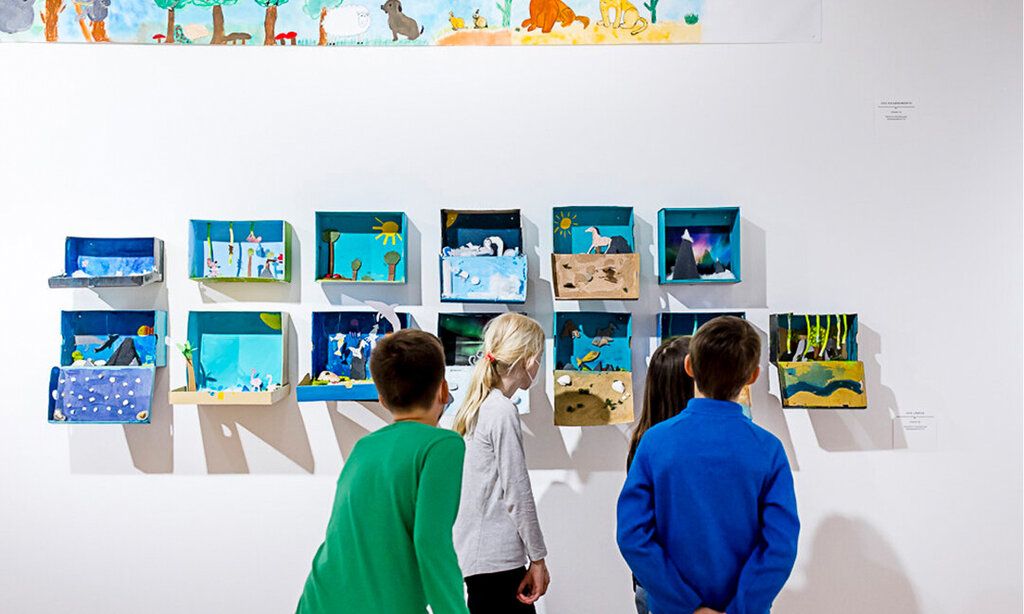 Kinder stehen vor selbstgemachten Kunstwerken, die an der wand hängen und betrachten die