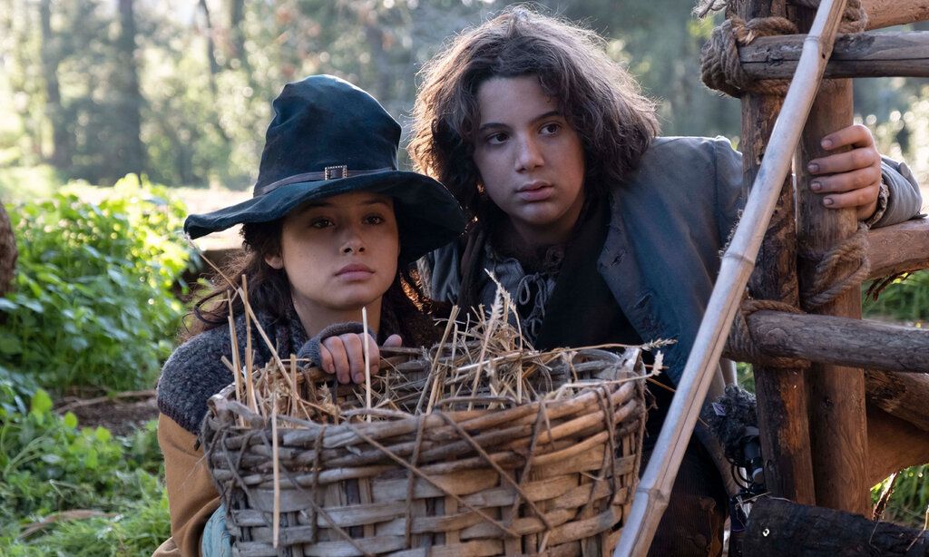 Mädchen mit Hexenhut und Junge in mittelalterlicher Kleidung hinter Weidenkorb, draußen