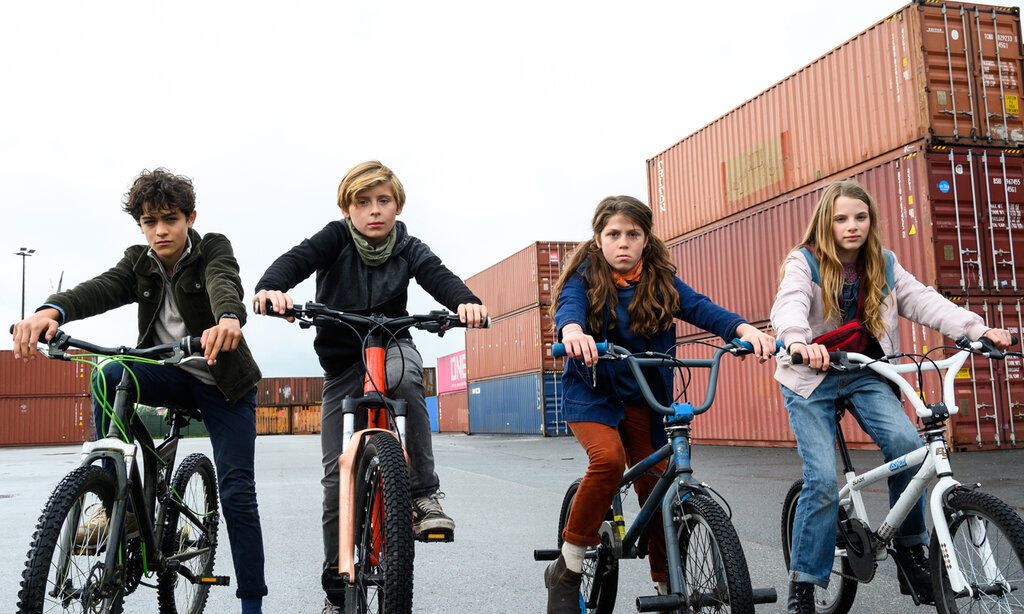 Zwei Jungs und zwei Mädchen auf BMX-Rädern zwischen Schiffs-Containern, in einem Hafengebiet