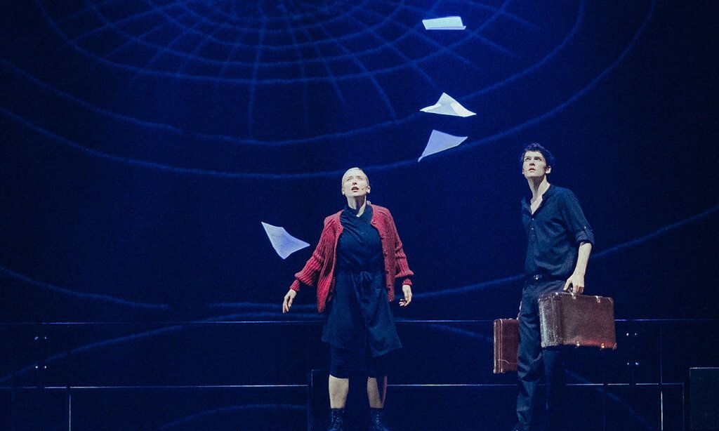 Szene mit Alex Melcher und Vera Bolten, Papierblätter fallen von oben herab, die beiden Personen gucken nach oben, die Bühne ist dunkel