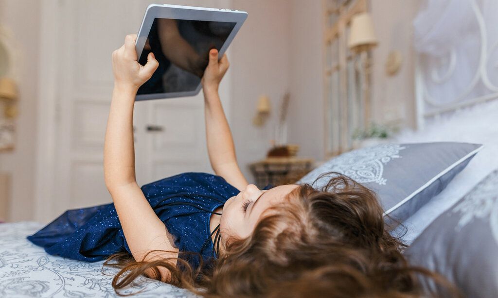 ein kleines Mädchen liegt auf dem Bett und hält ein Tablet in den Händen