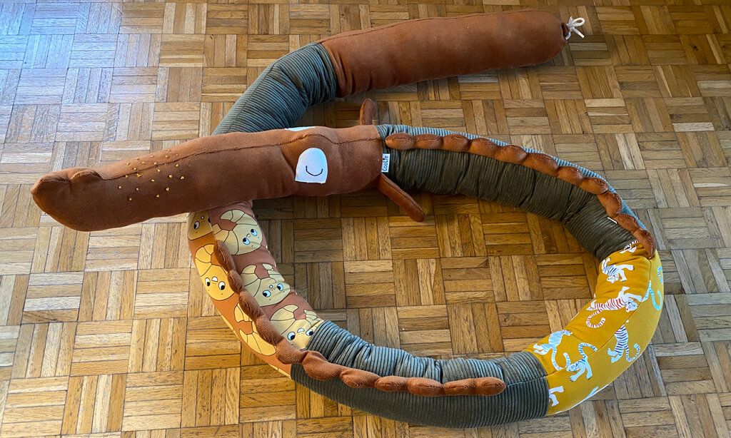 Selbstgenähtes Stillkissen in Form von einer Schlange, liegt auf Parkettboden