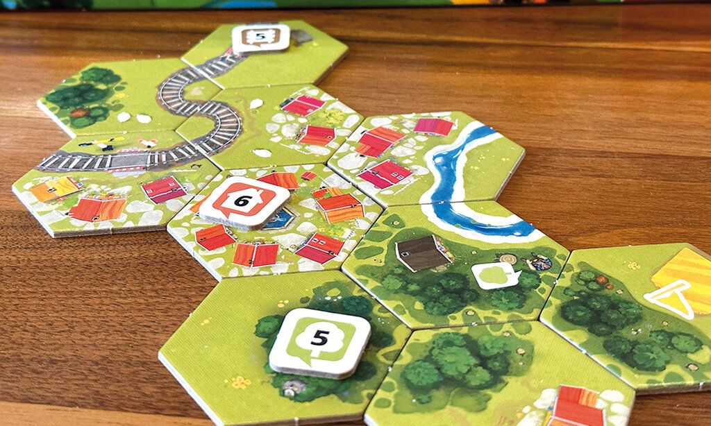 Spielszene von Dorfromantik, sechseckige Spielkarten liegen auf einem Tisch