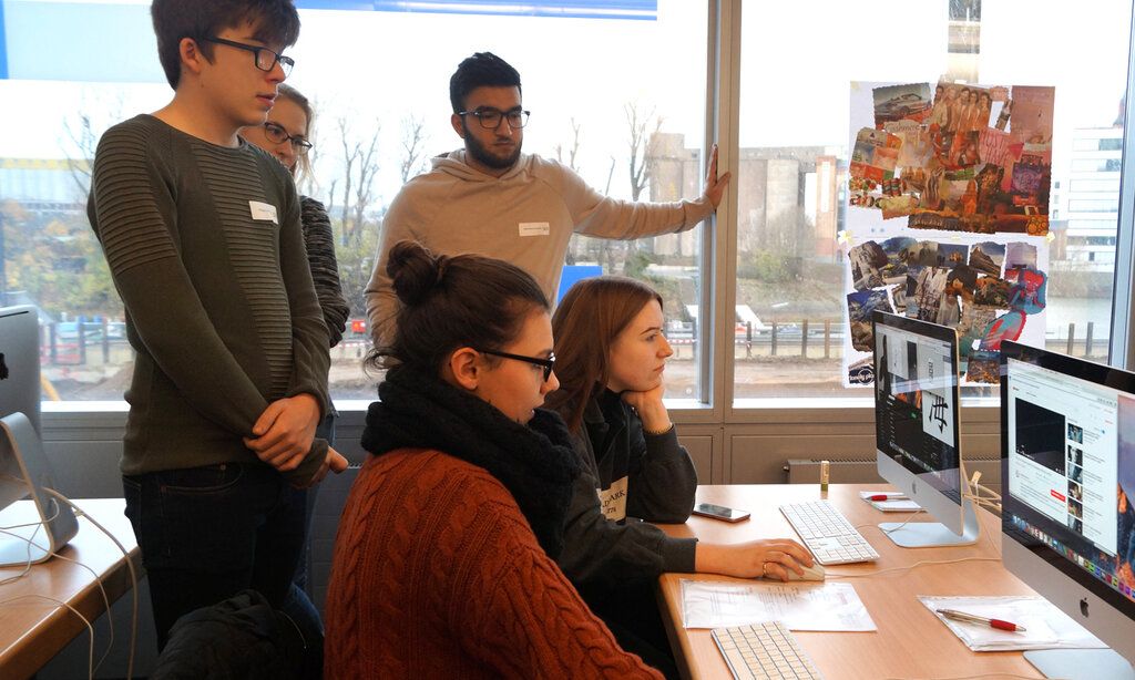 zwei Jugendliche sitzen an einem Schreibtisch und arbeiten an Computern, drei Jugendliche stehen dahinter und gucken zu, Düsseldorfer Jugendmedientage
