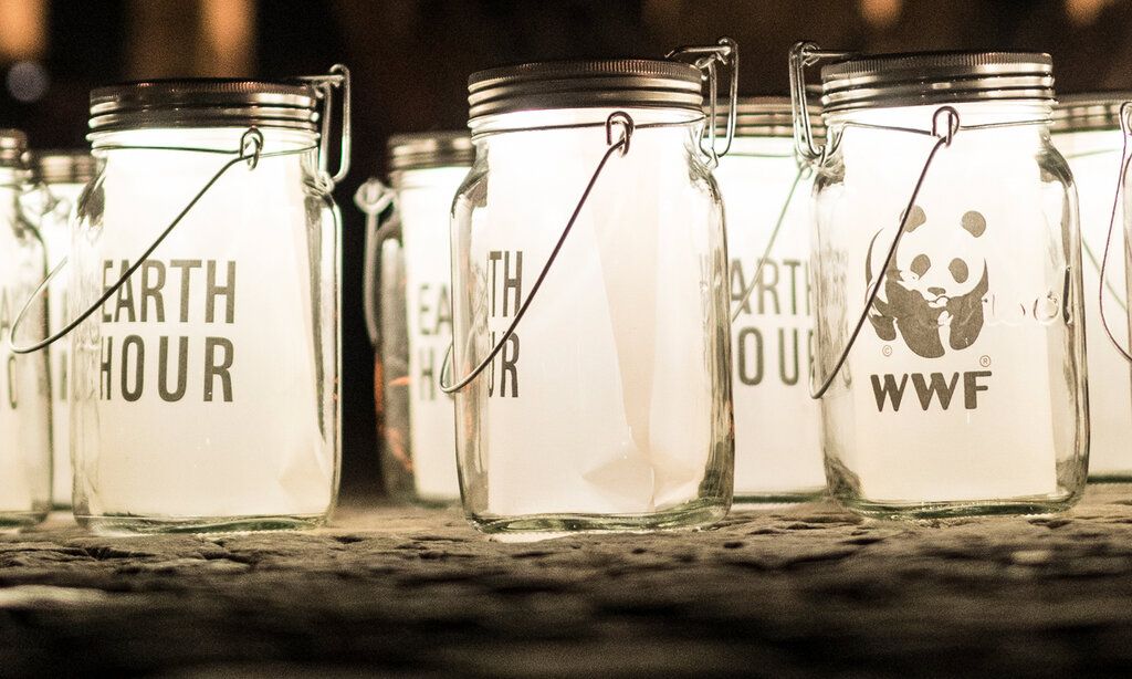 leuchtende Einmachgläser mit dem Schriftzug Earth Hour und dem WWF-Logo im Dunklen, im Hintergrund unscharf: das Brandenburger Tor