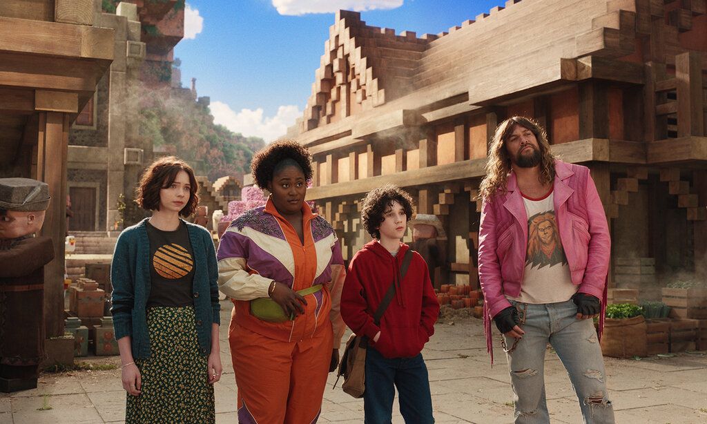 Szene aus dem Film Ein Minecraft Film, zwei Frauen, ein Junge und ein Mann stehen in einer Minecraft-Stadt
