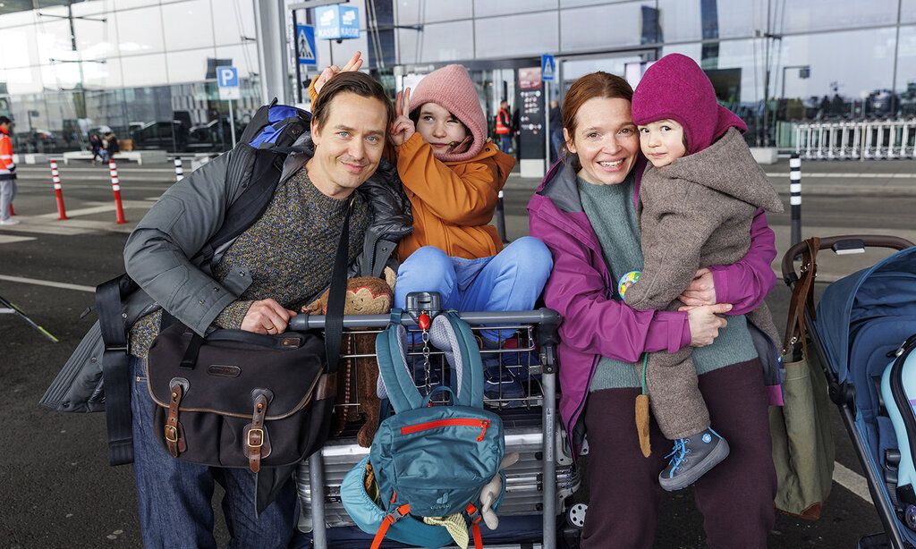 Vater, Mutter und zwei Kinder mit Kofferwagen und Gepäck an einem Flughafen