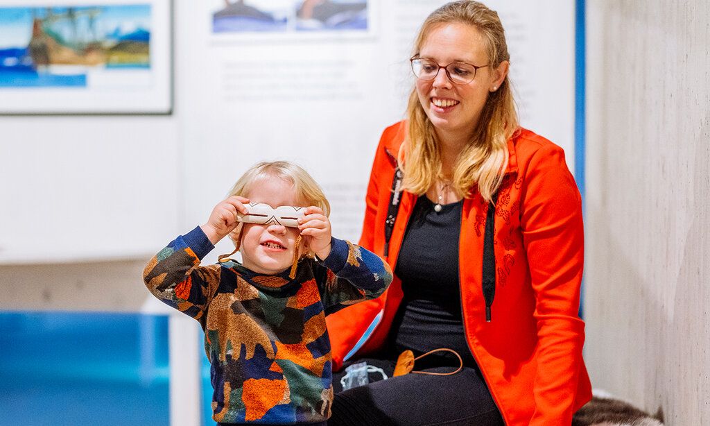 Kind hält sich eine Schneebrille vor die Augen, Frau sitzt dahinter