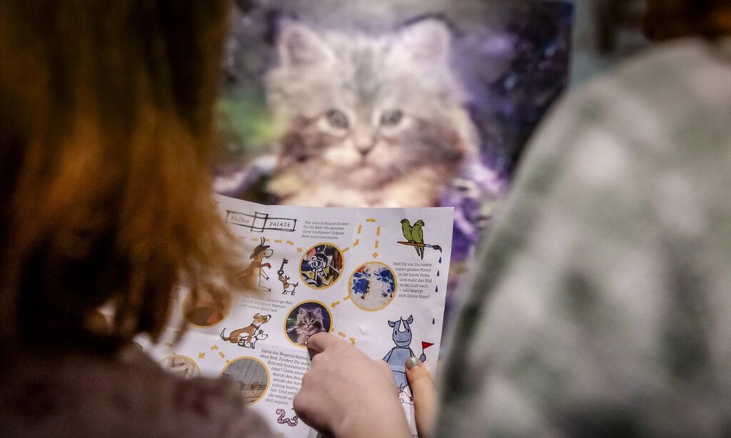 Personen gucken ins Entdeckerheft zu Monet, Cezanne, Matisse vom Kunstpalast, im Hintergrund ein Katzenbild