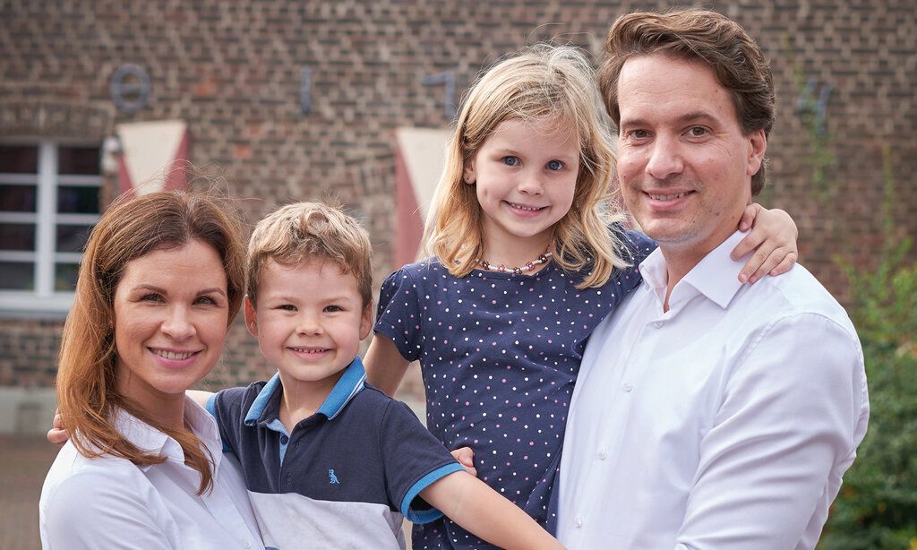 Familie Groß vor einem Haus in Unterrath, die Mutter hat den Sohn auf dem Arm und der Vater trägt die Tochter