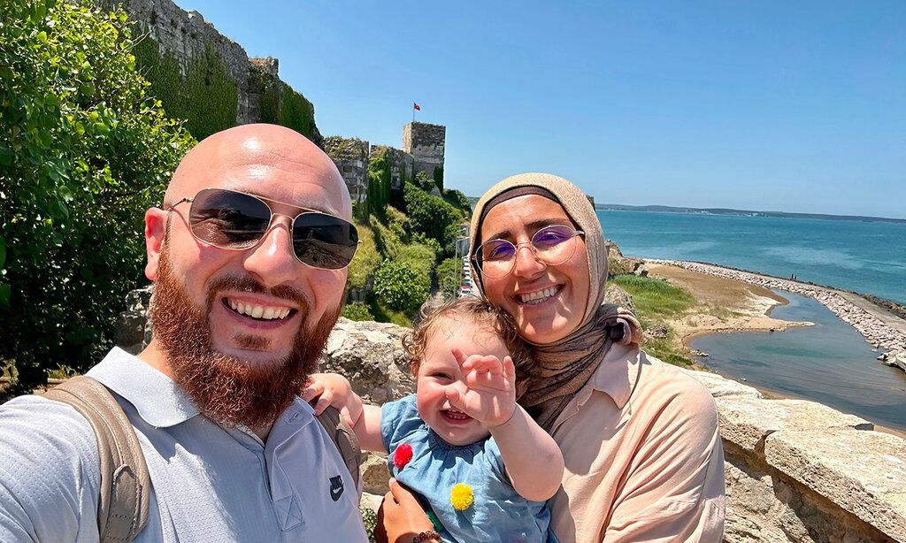 Vater und Mutter mit Baby vor einer bewachsenen Ruine am Meer
