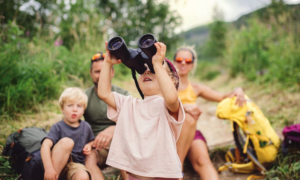 Familie macht Rast bei einer Wanderung, kleines Mädchen guckt in ein Fernglas