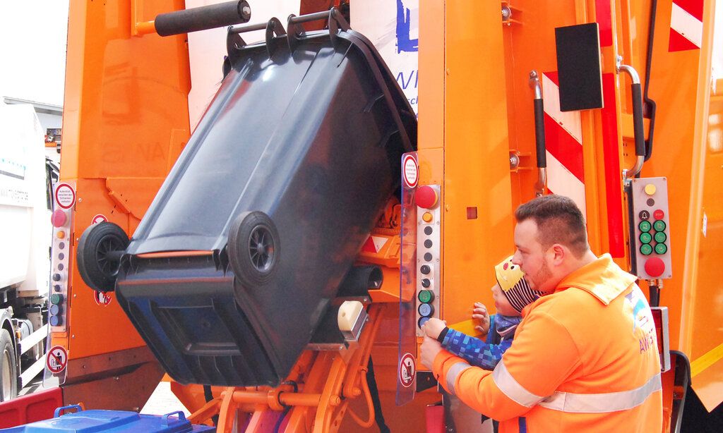 Kleiner Junge und Awista-Mitarbeiter leeren Mülltonne in Müllwagen gemeinsam mit Hydraulik