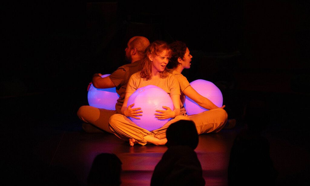 Familienmusikwoche Himmelblau, drei Personen mit rosa Wasserbällen auf der dunklen Bühne