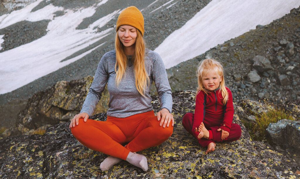 Mutter und Tochter sitzen in karger Berglandschaft im Schneidersitz und machen Yoga