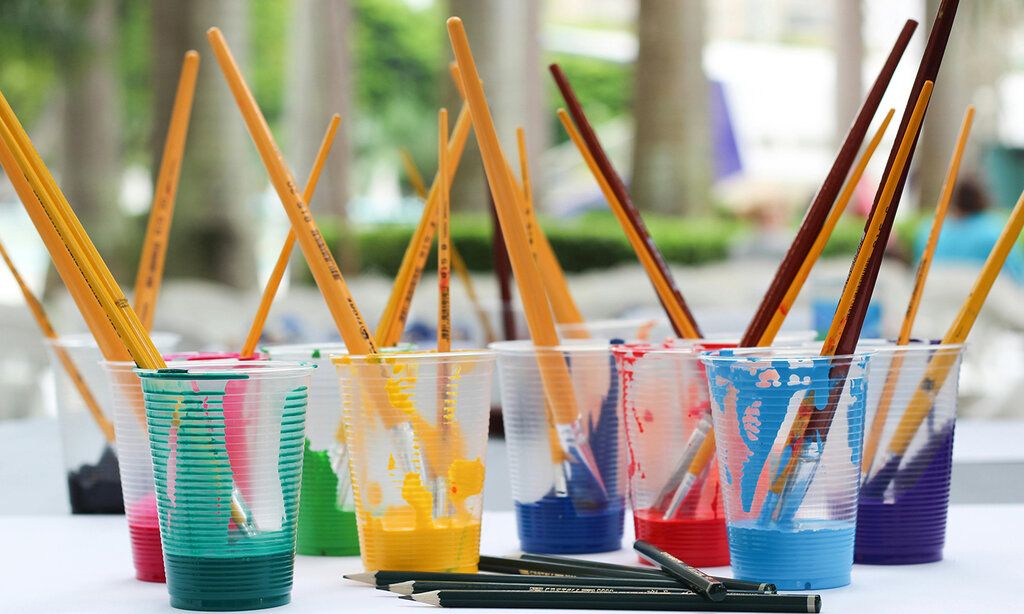 verschiedene Plastikbecher mit bunter Farbe und Pinseln