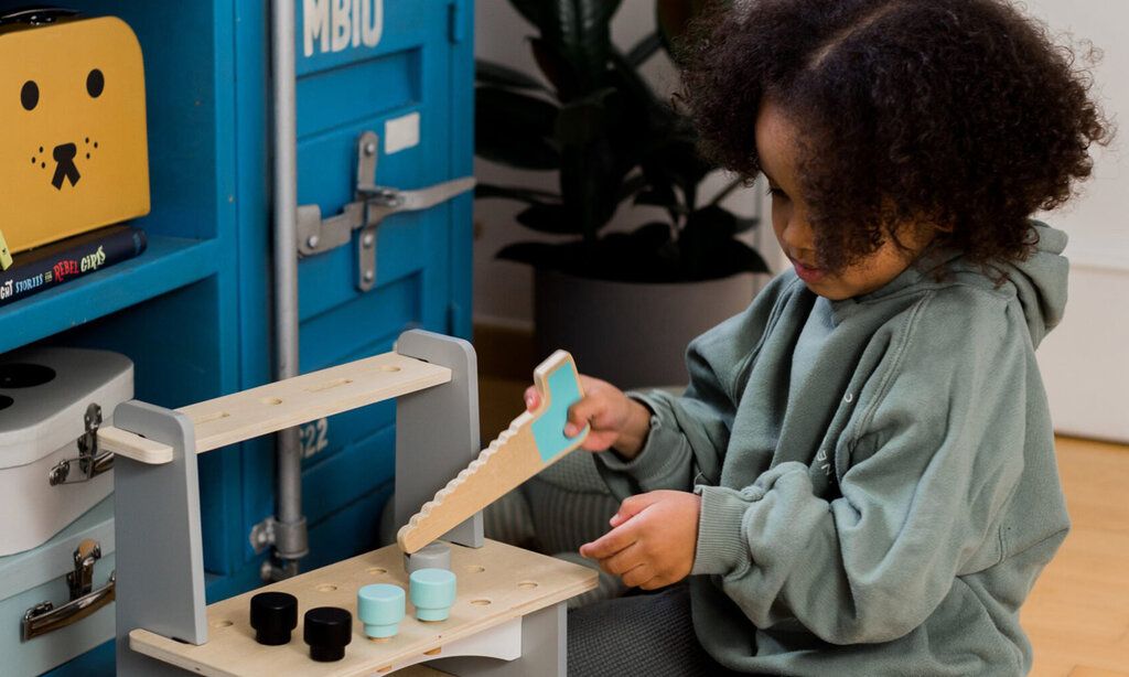 Mädchen spielt mit einer Spielzeug-Säge an einer Spielzeug-Werkbank