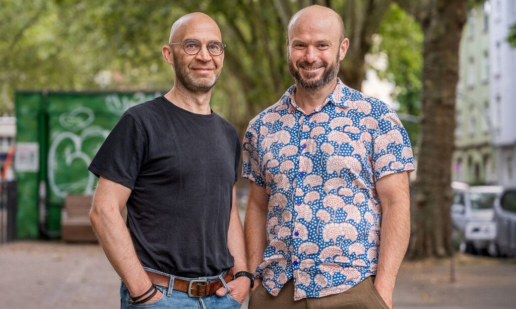 Porträt von Frank Walber und Markus Feger, im Hintergrund ein Platz in Düsseldorf mit Bäumen