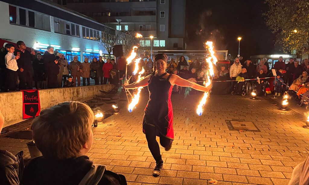 eine Frau läuft mit Fackeln in den Händen auf einem Platz in Düsseldorf-Garath, Leute schauen zu