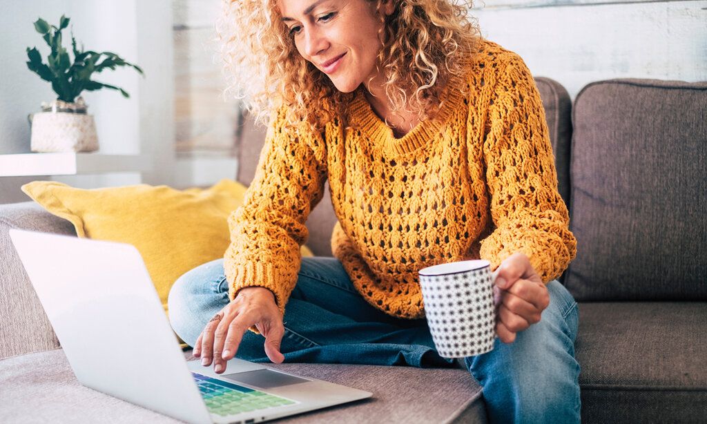 Frau mit Laptop und Kaffeetasse auf dem Sofa