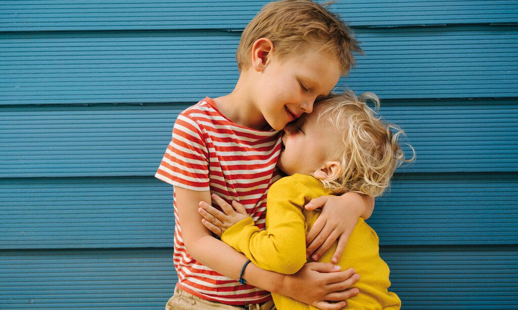 Zwei Jungs umarmen sich, im Hintergrund: blaue Wand