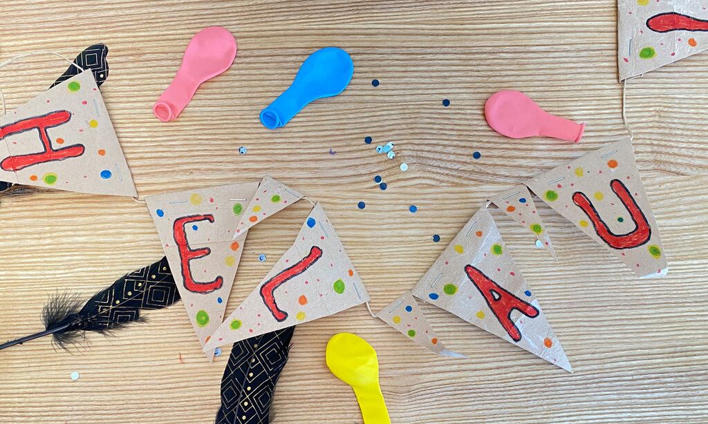 Girlande auf der „Helau“ steht, liegt auf Holzuntergrund, daneben Federn, Luftballons und Pailletten