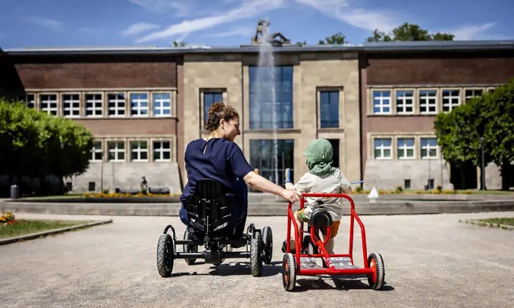 eine Mutter auf einem Gocart mit Kind auf einem Dreirad vorm Kunstpalast