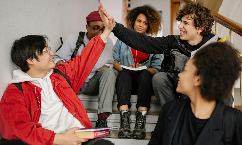 Gruppe Jugendliche sitezn in einem Treppenhaus, zwei machen High Five
