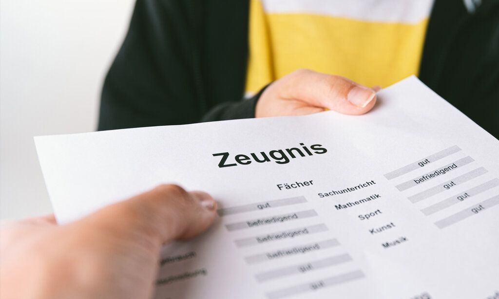 Hand eines Erwachsenen nimmt das Schulzeugnis eines Kindes